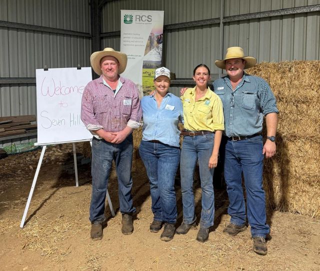 Photo of two women and two men in jeans and workshirts in front of hay bales in a shed